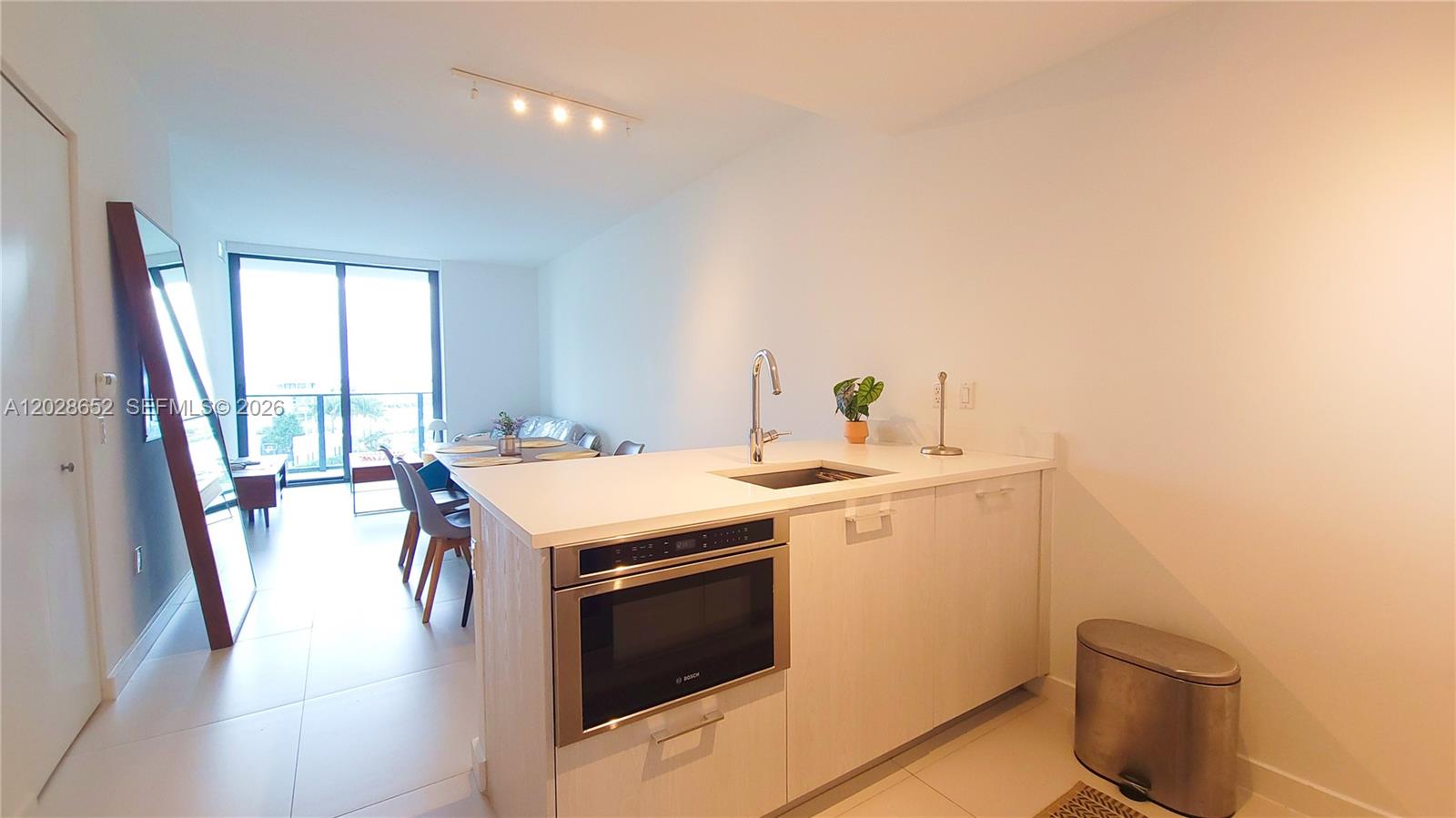 A modern kitchen island with a built-in microwave faces a dining area and balcony — 501 NE 31st St # 1002, Miami FL 33137, MIAMI, FL