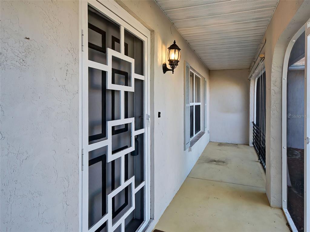 A covered entryway features a white security door with geometric patterns and a wall-mounted light — 1321 WASHINGTON DRIVE, ENGLEWOOD, FL