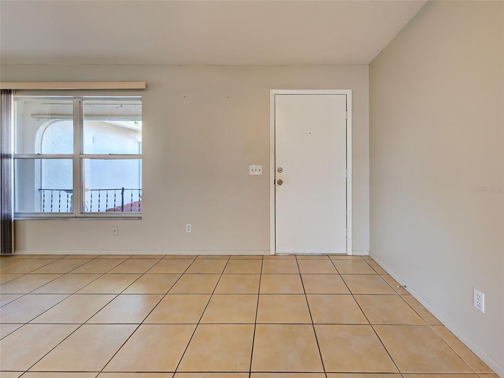 An empty room with beige tile flooring, a window, and a white entry door — 1321 WASHINGTON DRIVE, ENGLEWOOD, FL