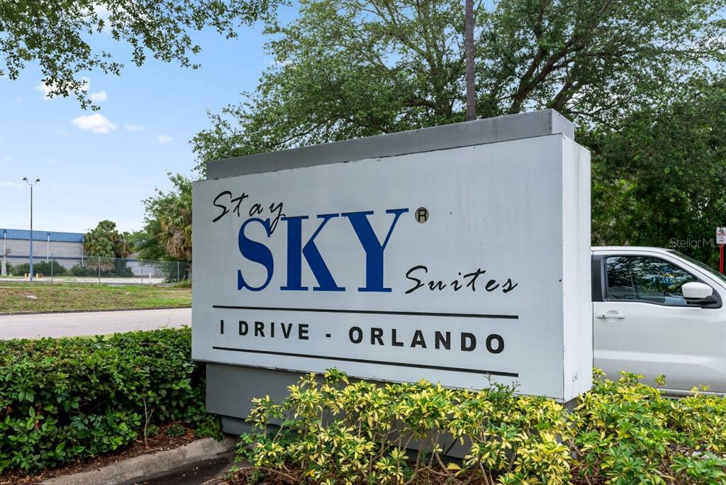 A white monument sign for Stay Sky Suites stands in front of green landscaping — 7601 CANADA AVENUE UNIT 221, ORLANDO, FL