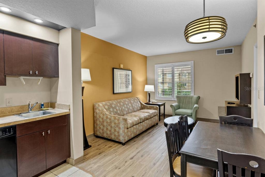 A living room with a kitchenette, dining table, floral sofa, and light wood flooring — 7601 CANADA AVENUE UNIT 221, ORLANDO, FL