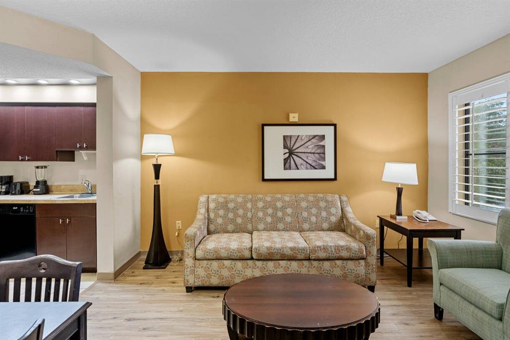 A living room features a floral sofa, a round coffee table, and an adjacent kitchen area — 7601 CANADA AVENUE UNIT 221, ORLANDO, FL
