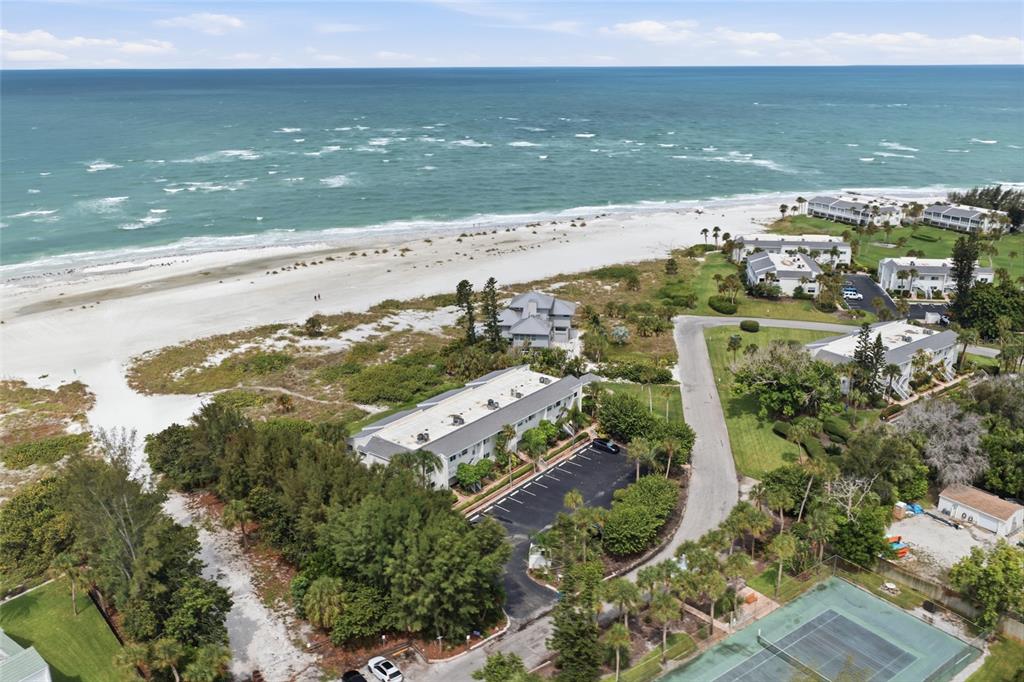 An aerial view shows a beachfront residential complex with white sand and turquoise water — 7001 GULF OF MEXICO DRIVE UNIT 24, LONGBOAT KEY, FL