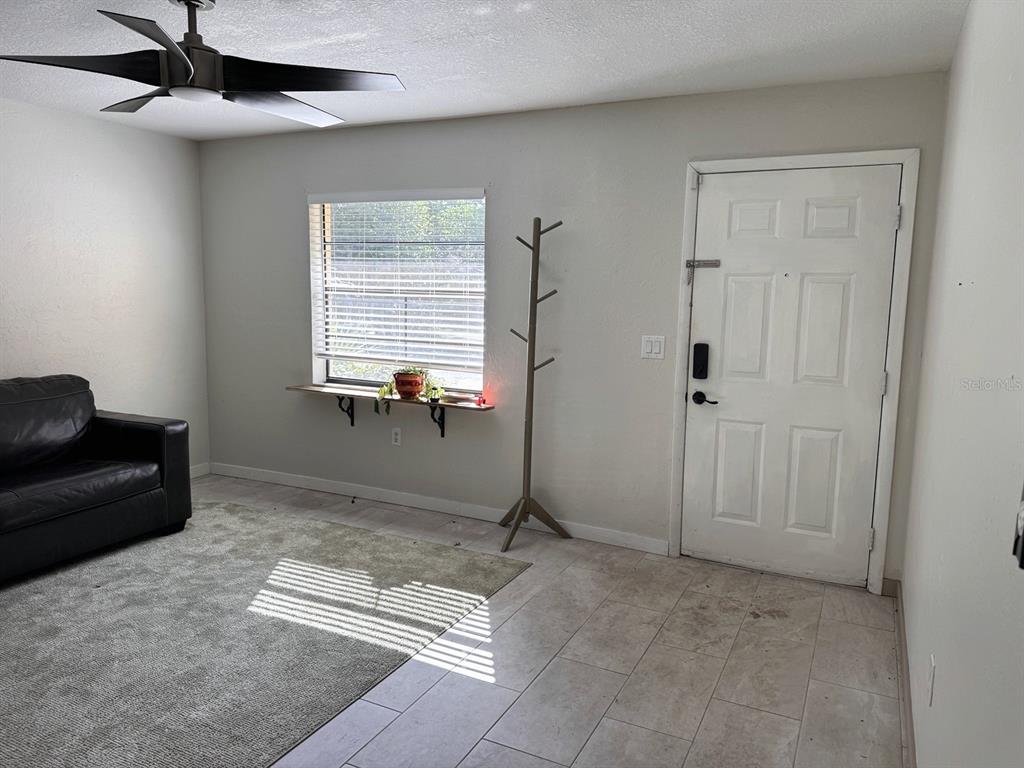A living room features a black leather sofa, a coat rack, and a front door — 3414 NW 21ST DRIVE UNIT E4, GAINESVILLE, FL