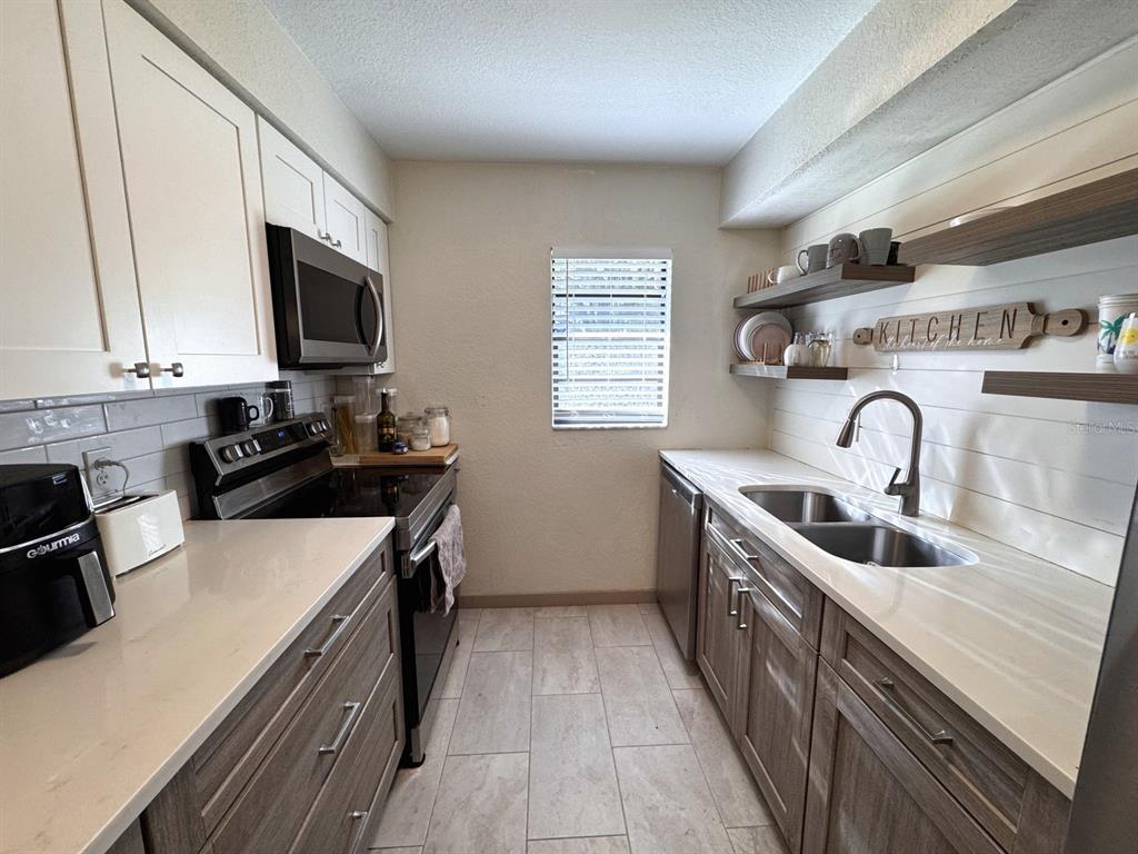 A galley kitchen features white upper cabinets, wood-toned lower cabinets, quartz countertops, and open shelving — 3414 NW 21ST DRIVE UNIT E4, GAINESVILLE, FL