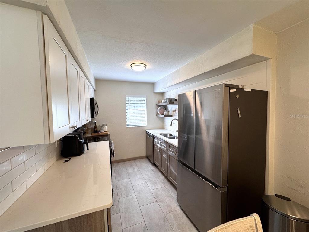 A galley kitchen features white upper cabinets, wood-toned lower cabinets, stainless steel appliances, and tile flooring — 3414 NW 21ST DRIVE UNIT E4, GAINESVILLE, FL