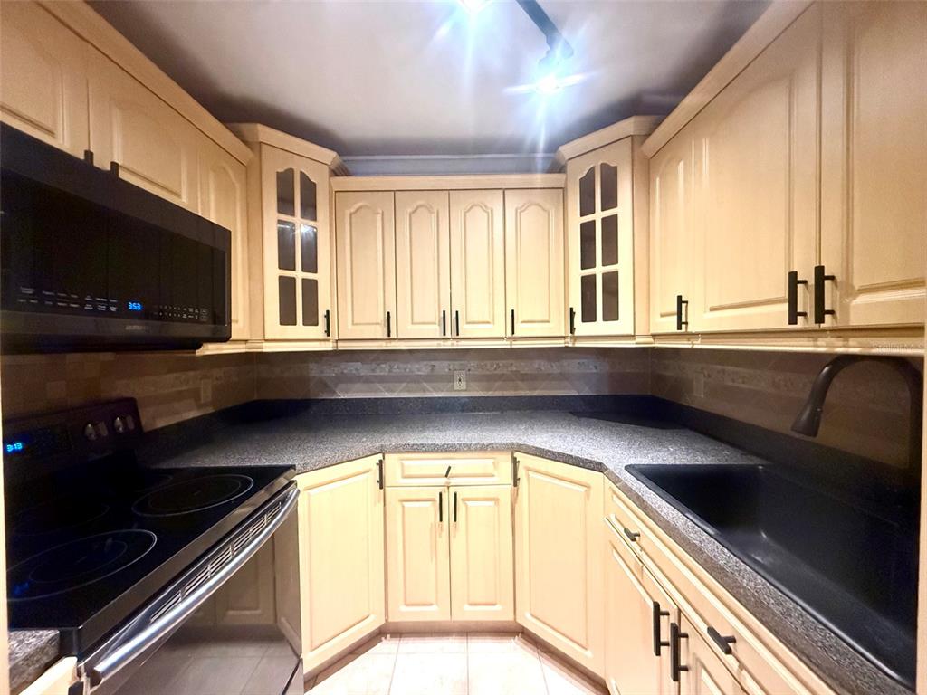 A kitchen features cream-colored cabinets, dark countertops, a black microwave, and a black sink — 926 LAKE DESTINY ROAD UNIT F, ALTAMONTE SPRINGS, FL