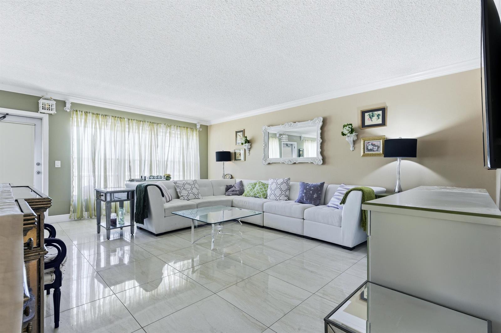 A living room features a white sectional sofa, glass coffee table, and light tile flooring — 213 Wellington E, West Palm Beach FL 33417, WEST PALM BEACH, FL