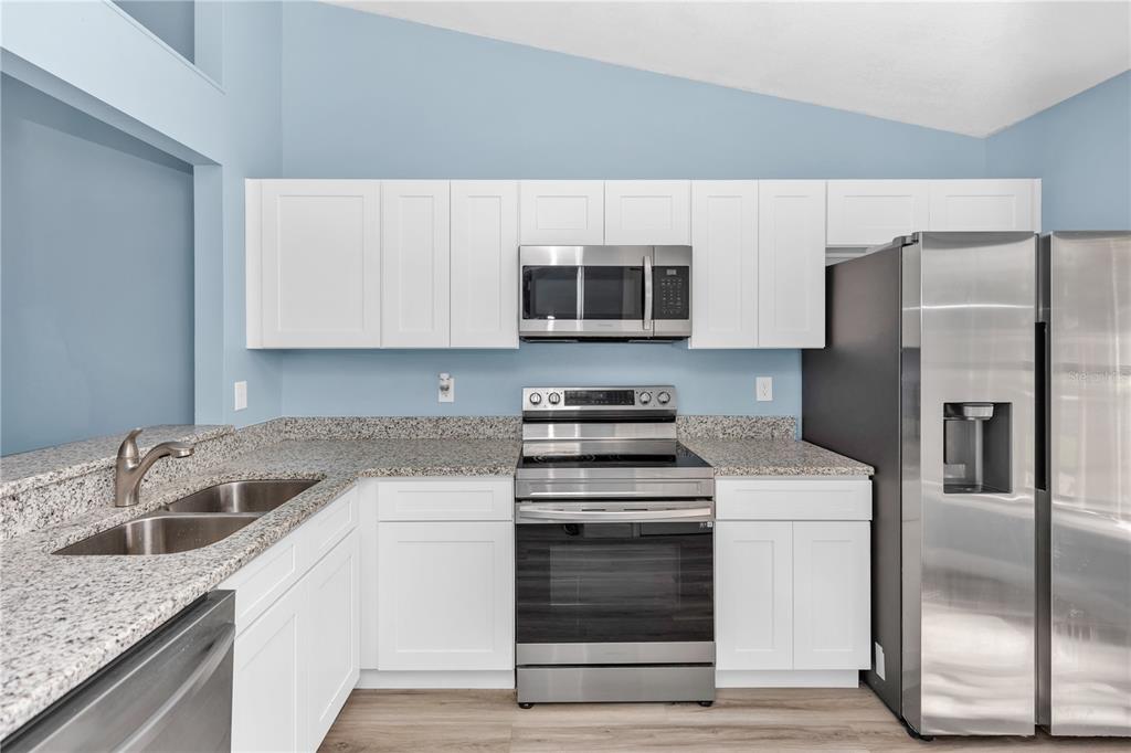 A kitchen features white cabinets, granite countertops, and stainless steel appliances against light blue walls — 2501 KING OAK CIRCLE, ST CLOUD, FL
