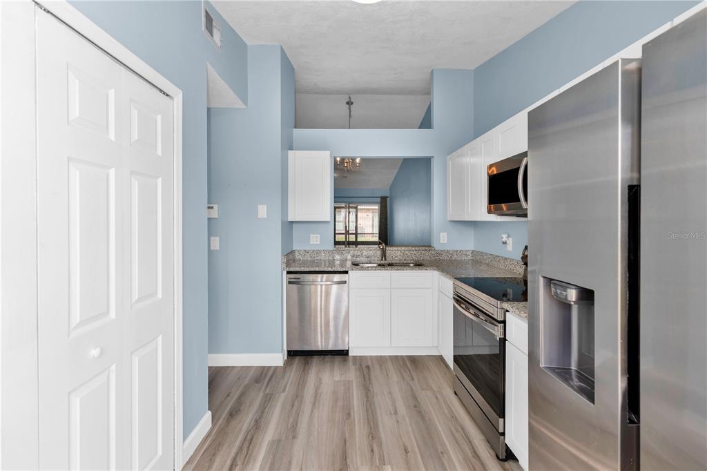 A kitchen features white cabinets, stainless steel appliances, granite countertops, and light wood-look flooring — 2501 KING OAK CIRCLE, ST CLOUD, FL