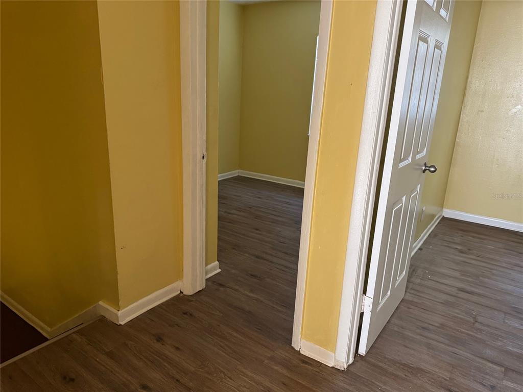 A hallway with yellow walls and wood-look flooring leads into an adjacent room — 1109 PHELPS STREET, JACKSONVILLE, FL