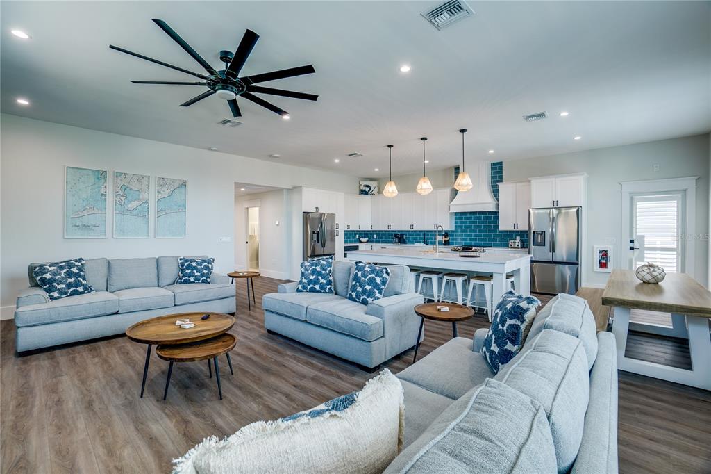 An open-concept living room and kitchen feature light gray sofas, wood flooring, and blue tile — 2102 AVENUE B, BRADENTON BEACH, FL