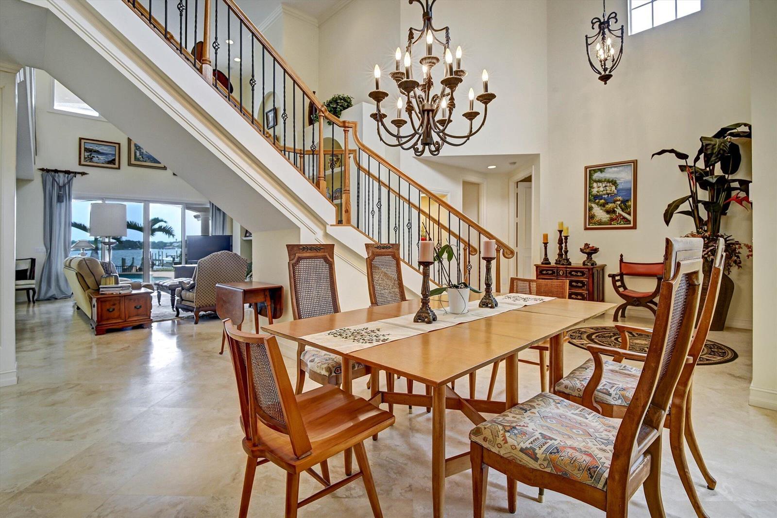 A dining area with a wooden table and chairs sits beneath a staircase and chandelier — 881 SE Saint Lucie Boulevard, Stuart FL 34996, STUART, FL