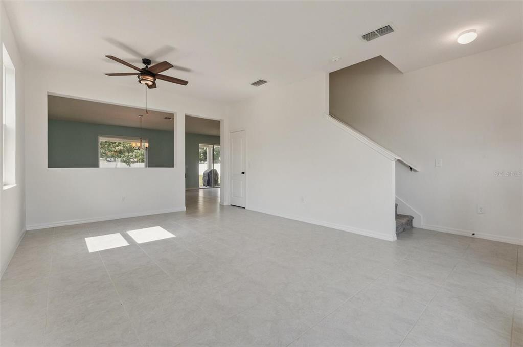 An empty room with white walls, tile flooring, a ceiling fan, and a staircase — 15898 BRADICKS COURT, CLERMONT, FL