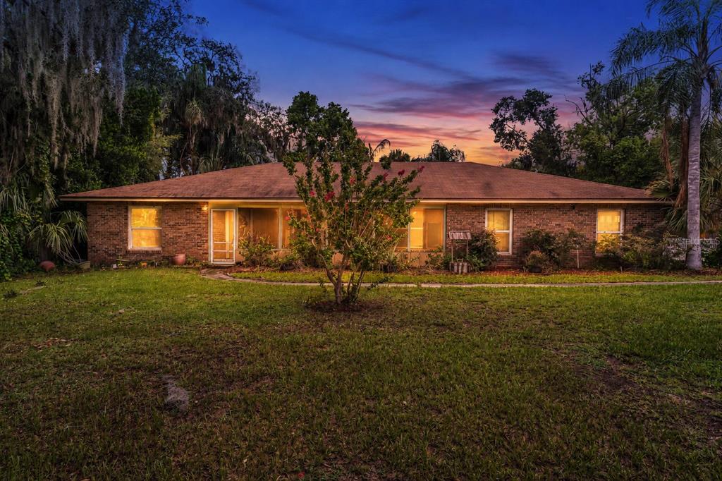 A single-story brick house with a screened porch sits on a grassy lawn at dusk — 130 SLADE DRIVE, LONGWOOD, FL