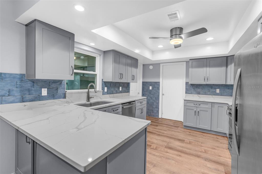 A kitchen features gray cabinets, white marble-look countertops, blue tile backsplashes, and wood-look flooring — 130 SLADE DRIVE, LONGWOOD, FL