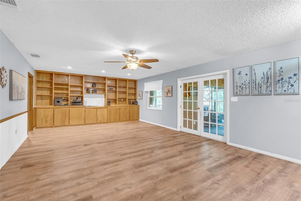 A living room features wood-look flooring, a built-in wooden bookshelf, a ceiling fan, and French doors — 130 SLADE DRIVE, LONGWOOD, FL