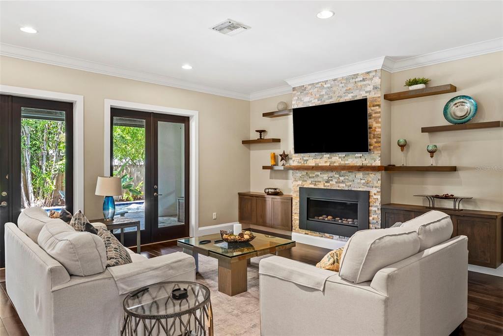 A living room features a stone fireplace, wall-mounted television, floating shelves, and two beige sofas — 3211 W BAY VILLA AVENUE, TAMPA, FL