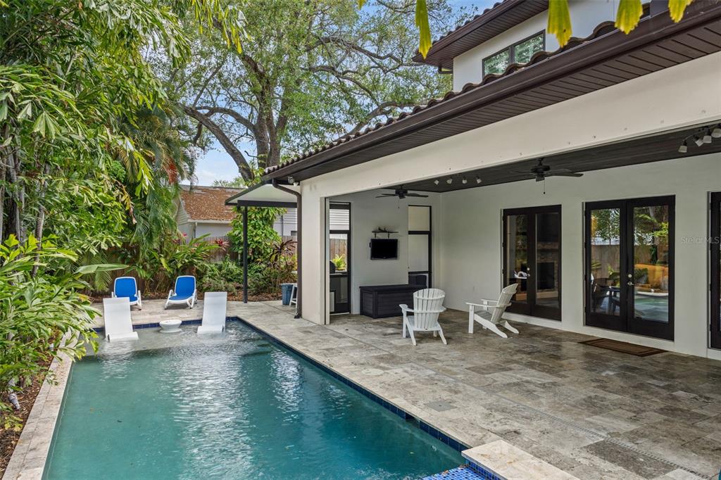 A covered patio with stone flooring overlooks a swimming pool with lounge chairs — 3211 W BAY VILLA AVENUE, TAMPA, FL