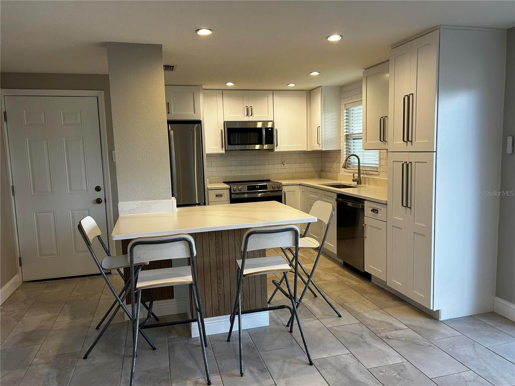 A kitchen features white cabinets, stainless steel appliances, a center island, and tiled flooring — 8802 BAY POINTE DRIVE UNIT 102, TAMPA, FL