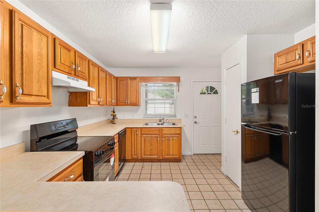 A kitchen with wood cabinets, laminate countertops, a black stove, and a black refrigerator — 11191 SE 55TH AVENUE ROAD UNIT 401, BELLEVIEW, FL