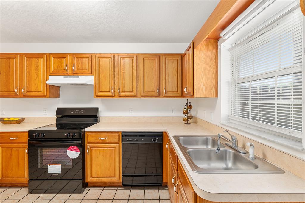 A kitchen with wood cabinets, black appliances, a double sink, and tiled flooring — 11191 SE 55TH AVENUE ROAD UNIT 401, BELLEVIEW, FL