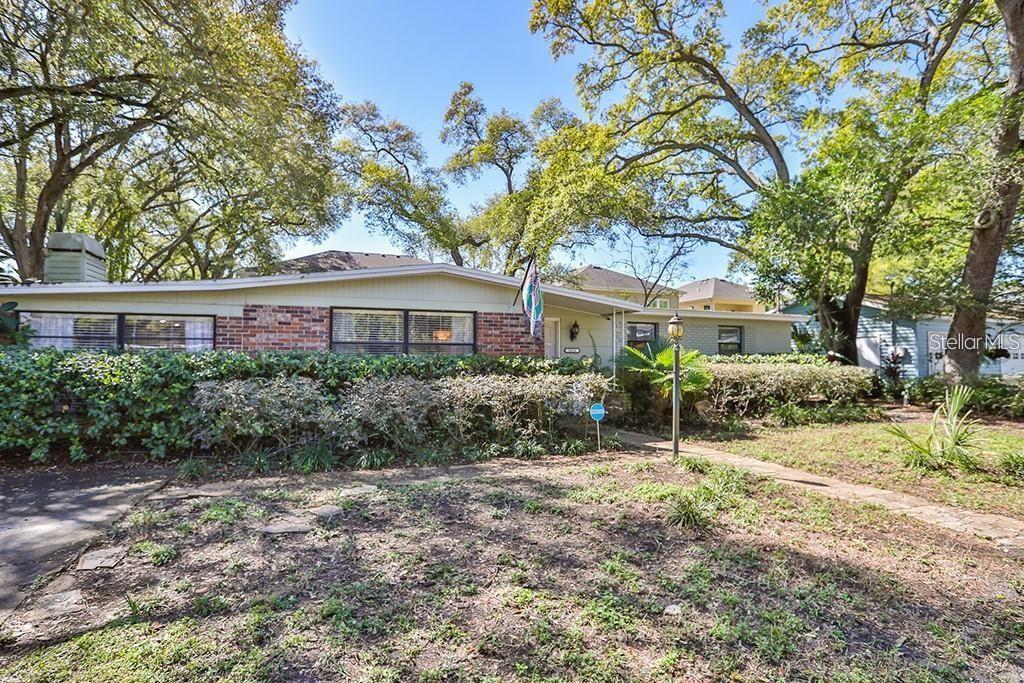 A single-story house with a brick and siding exterior sits behind a large, overgrown hedge — 3214 W COACHMAN AVENUE, TAMPA, FL