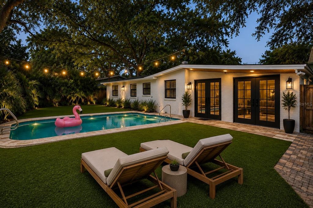 A backyard features a swimming pool with a pink flamingo float, lounge chairs, and string lights — 3214 W COACHMAN AVENUE, TAMPA, FL