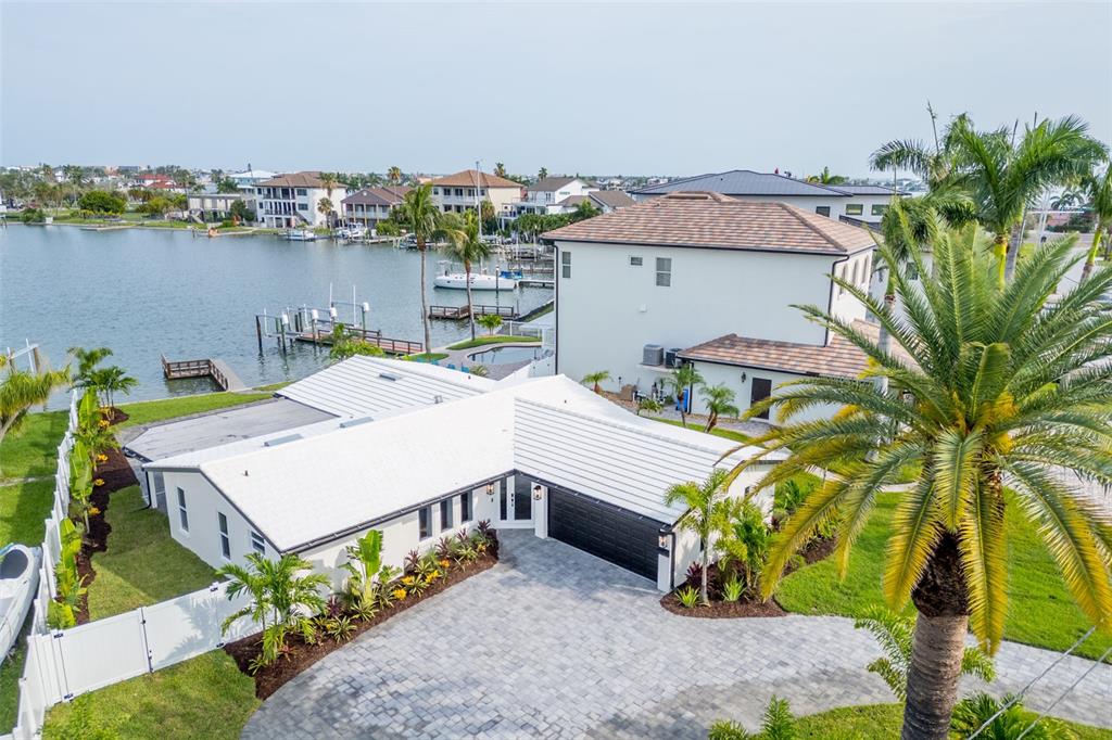 A white single-story house with a black garage door and a paved driveway near water — 10350 PARADISE BOULEVARD, TREASURE ISLAND, FL