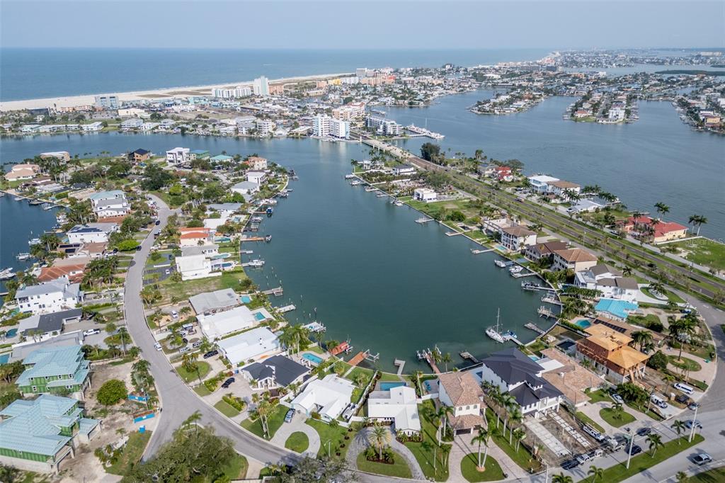An aerial view shows a white house with a black garage door and waterfront access — 10350 PARADISE BOULEVARD, TREASURE ISLAND, FL