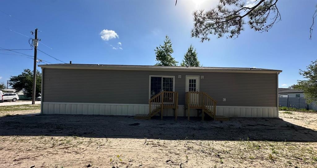 The exterior of a single-story manufactured home features gray siding, two wooden staircases, and sandy ground — 16136 CHANCAS STREET, BROOKSVILLE, FL