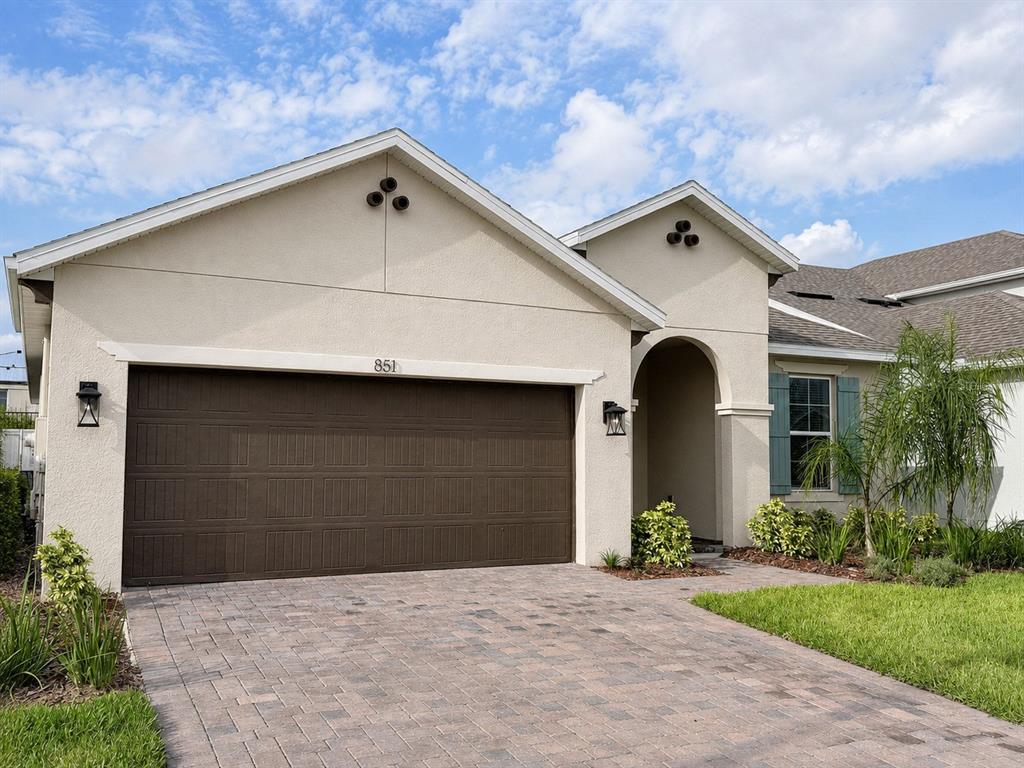 A single-story house exterior features a two-car garage, stucco walls, and a paved driveway — 851 VINEYARD RIDGE ROAD, MINNEOLA, FL