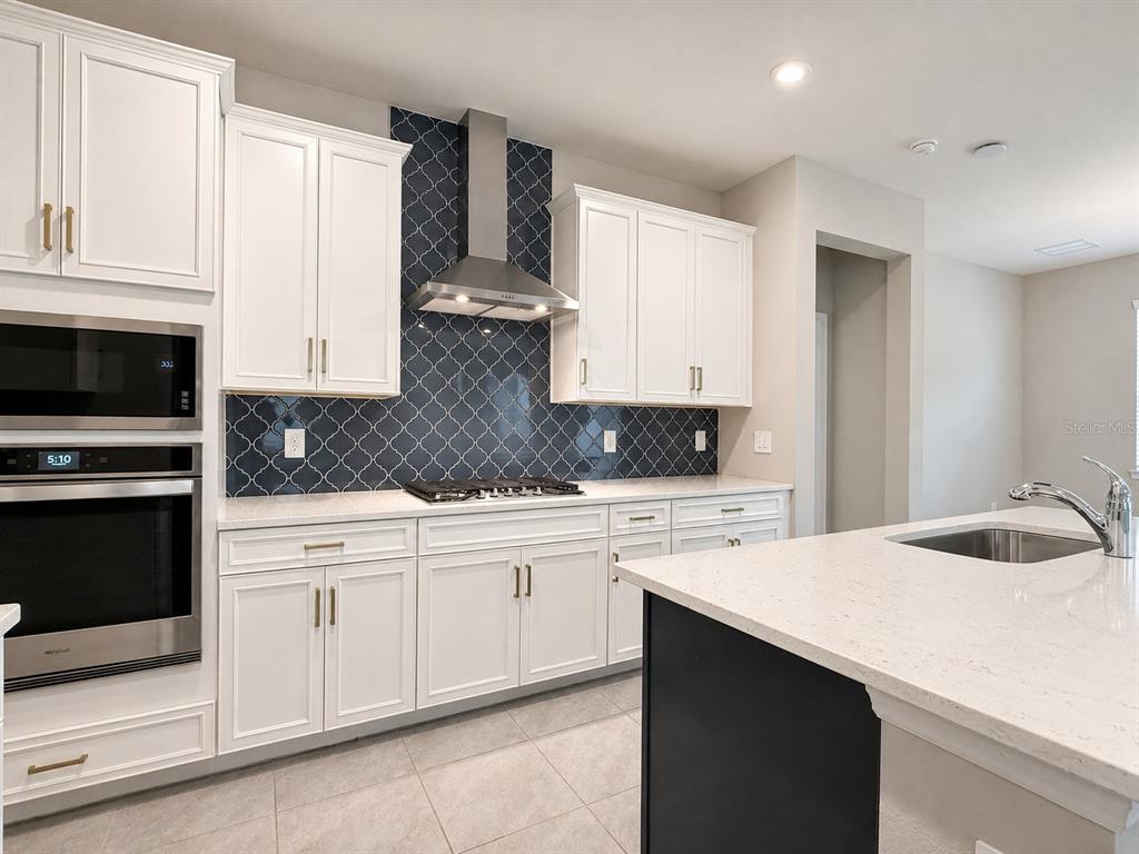 A kitchen features white cabinets, a dark blue arabesque tile backsplash, and a central island — 851 VINEYARD RIDGE ROAD, MINNEOLA, FL