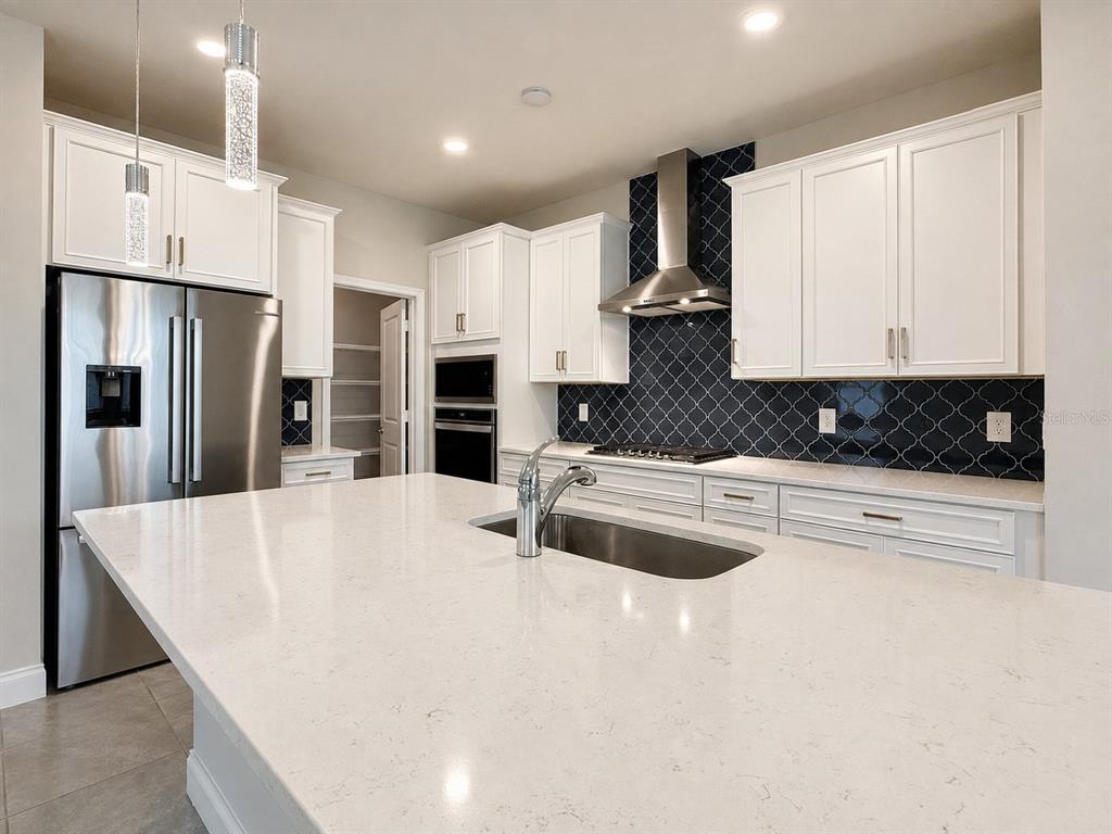 A modern kitchen features white cabinets, a large quartz island, and a dark patterned backsplash — 851 VINEYARD RIDGE ROAD, MINNEOLA, FL