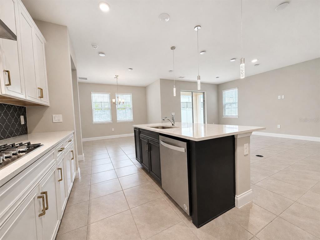 A kitchen features white upper cabinets, a dark island with a stainless dishwasher, and tile flooring — 851 VINEYARD RIDGE ROAD, MINNEOLA, FL