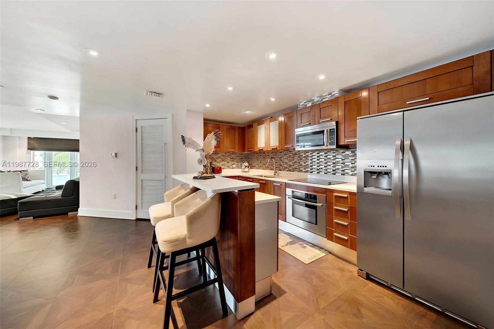 A kitchen features wood cabinets, stainless steel appliances, a breakfast bar, and dark wood flooring — 448 Ocean Dr # 302, Miami Beach FL 33139, MIAMI BEACH, FL