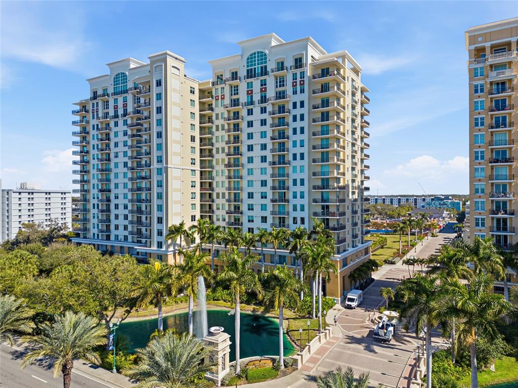 A tall residential building with balconies stands beside a pond with a fountain and palm trees — 800 N TAMIAMI TRAIL UNIT 1203, SARASOTA, FL