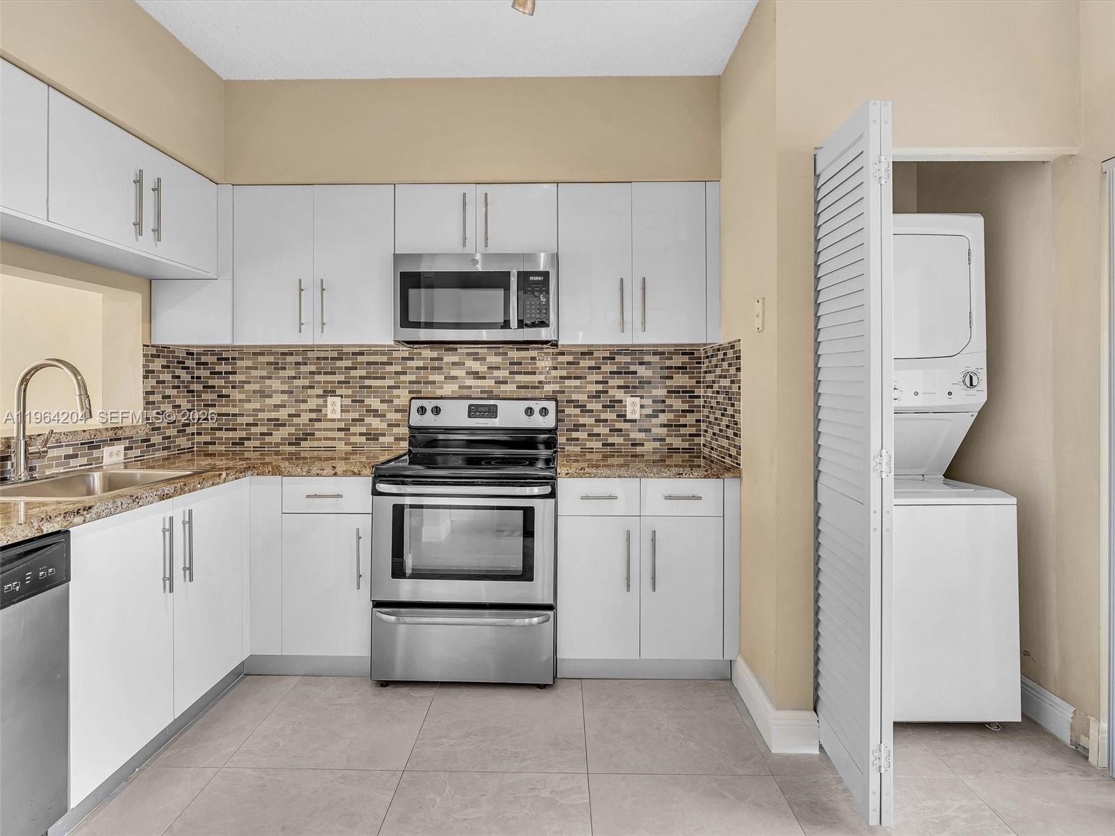 A kitchen features white cabinets, stainless steel appliances, a tiled backsplash, and a laundry closet — 60 Key West Ct # 60, Weston FL 33326, WESTON, FL