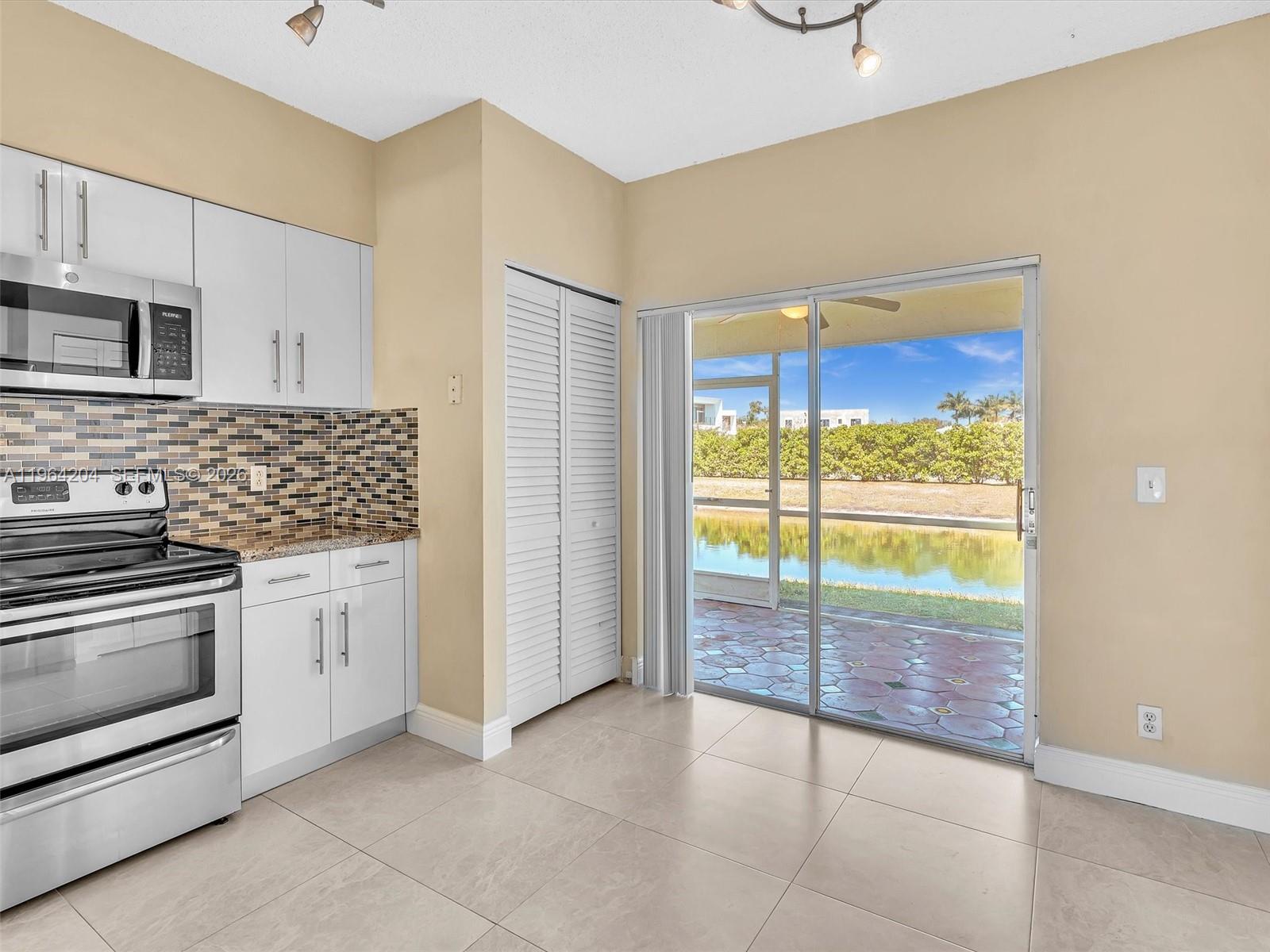 A kitchen with white cabinets and a sliding glass door overlooking a pond and patio — 60 Key West Ct # 60, Weston FL 33326, WESTON, FL