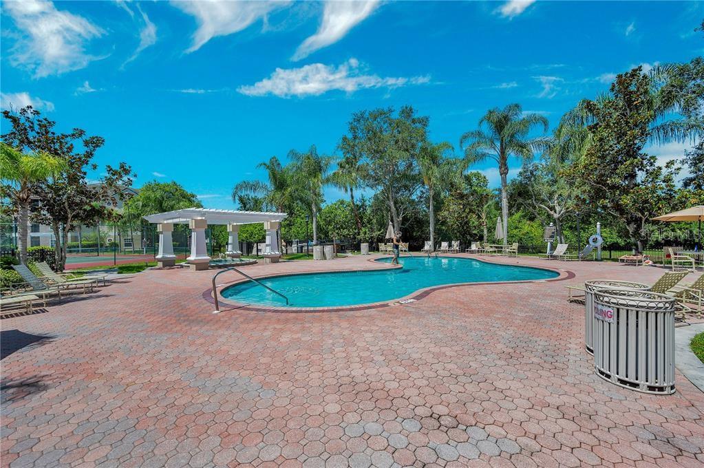 A swimming pool with a brick paver deck, lounge chairs, and a pergola under blue skies — 5174 NORTHRIDGE ROAD UNIT 211, SARASOTA, FL