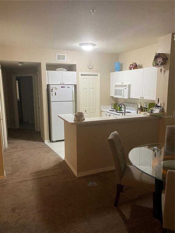 A kitchen with white cabinets, a refrigerator, and a breakfast bar overlooks a dining area — 5174 NORTHRIDGE ROAD UNIT 211, SARASOTA, FL