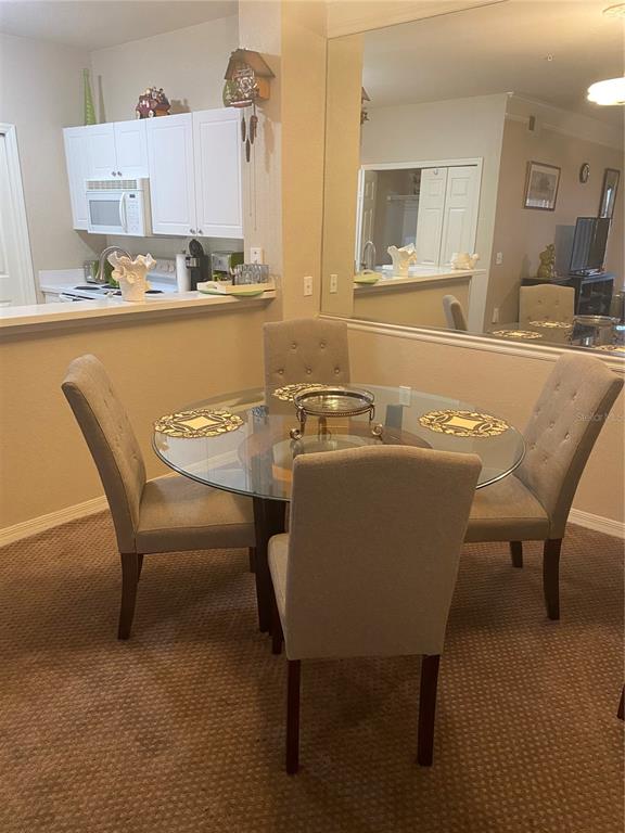 A dining area with a glass-topped table, four upholstered chairs, and a large wall mirror — 5174 NORTHRIDGE ROAD UNIT 211, SARASOTA, FL