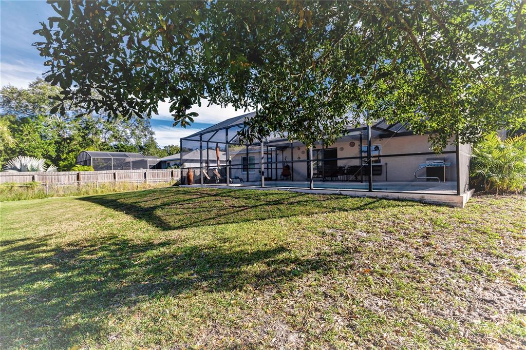 A backyard view of a house with a screened-in pool enclosure and a grassy lawn — 912 72ND STREET NW, BRADENTON, FL
