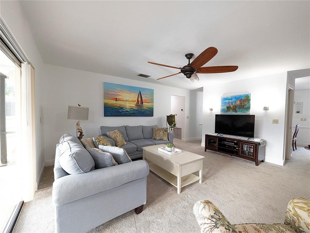 A living room features light blue sofas, a coffee table, a television, and a ceiling fan — 912 72ND STREET NW, BRADENTON, FL