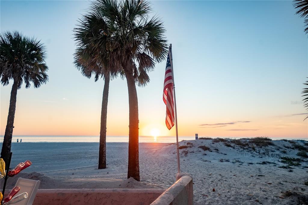 A beach view at sunset featuring palm trees, a sand dune, and an American flag — 130 177TH TER W, REDINGTON SHORES, FL