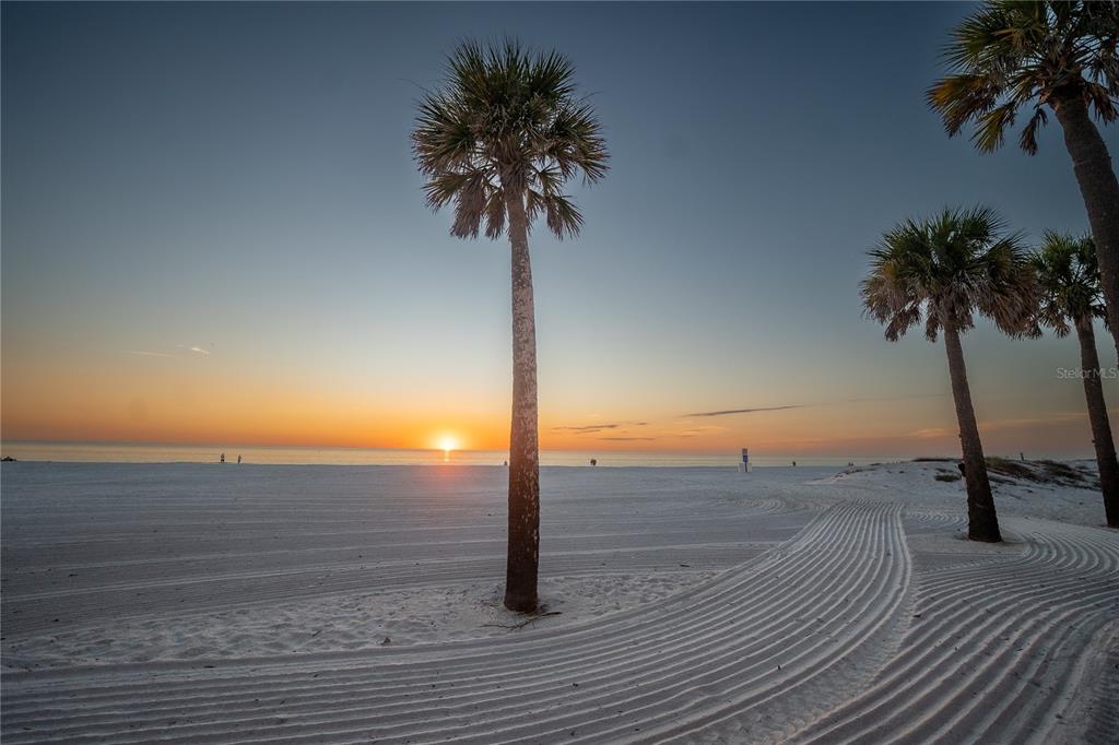 A sunset view over a white sand beach with several palm trees in the foreground — 130 177TH TER W, REDINGTON SHORES, FL