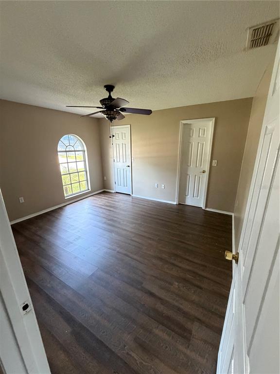 A bedroom features dark wood-look flooring, a ceiling fan, and an arched window — 7119 PEBBLE PASS LOOP, LAKELAND, FL