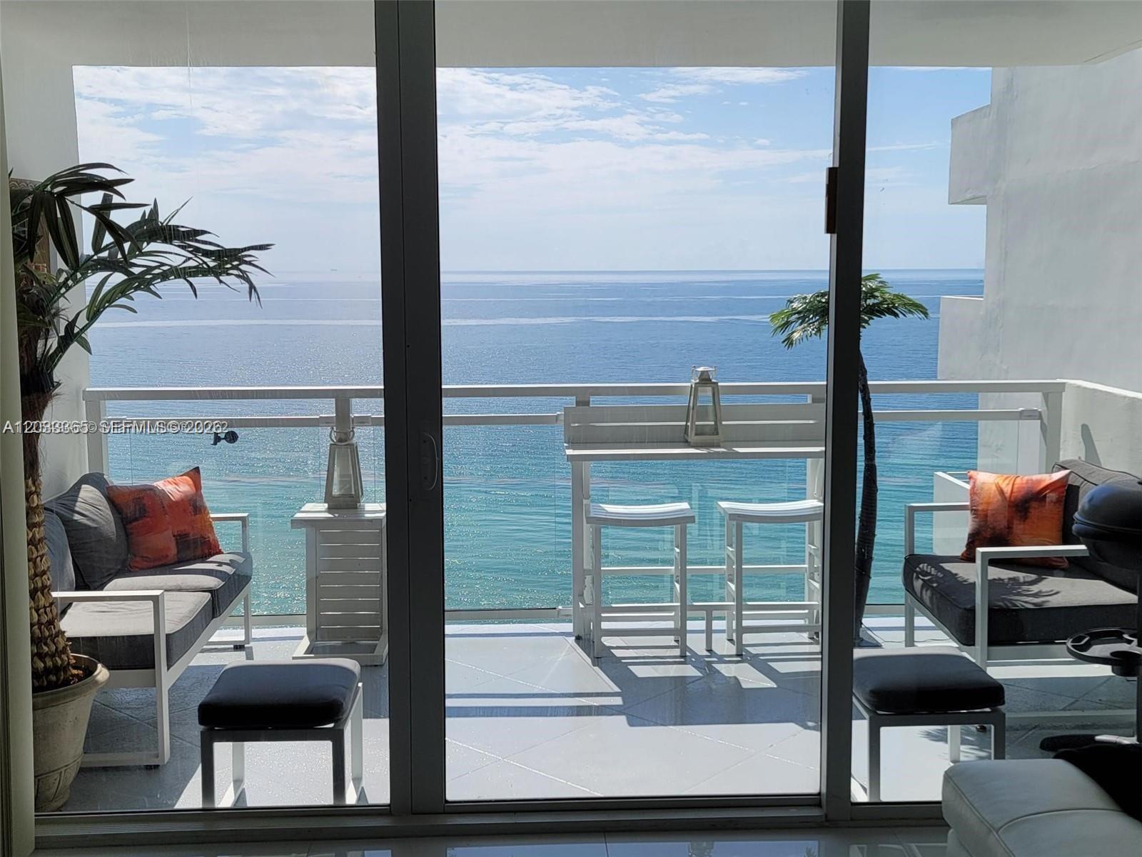 A balcony with outdoor furniture overlooks the ocean through a large sliding glass door — 2030 S Ocean Dr # 1815, Hallandale Beach FL 33009, HALLANDALE BEACH, FL