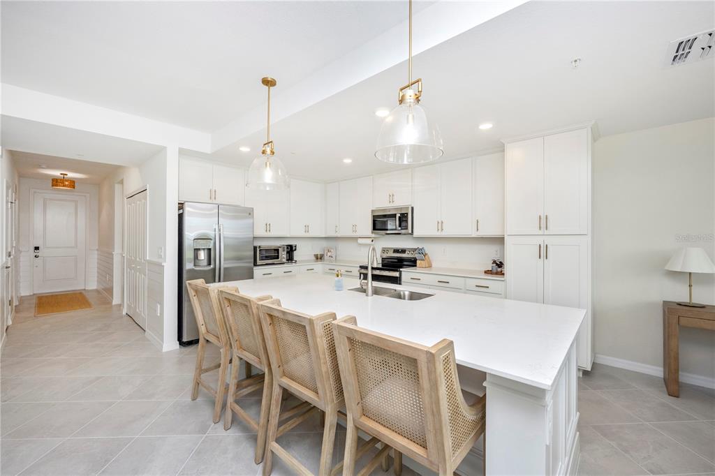 A bright kitchen features white cabinetry, a large quartz island with seating, and stainless appliances — 17625 OPAL SAND DRIVE UNIT 106, VENICE, FL