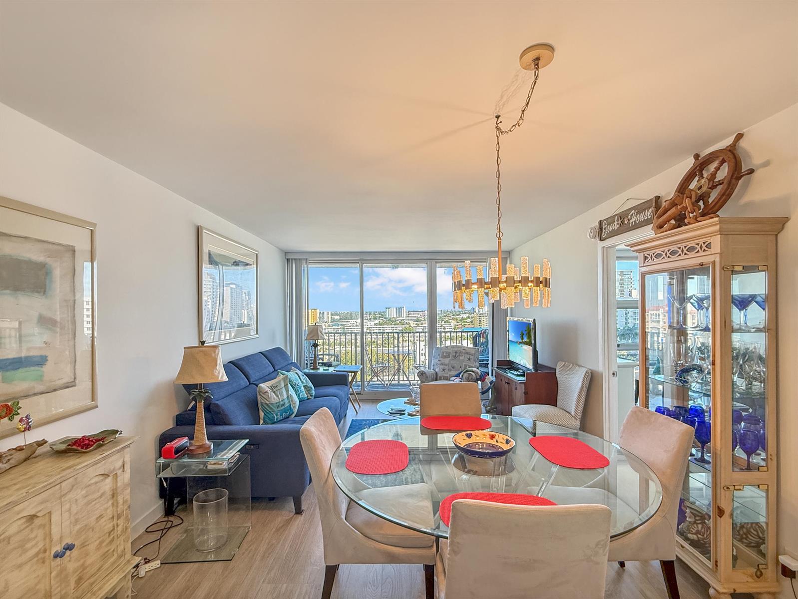 A living and dining area features a blue sofa, glass table, and a city view balcony — 531 N Ocean Boulevard # 1203, Pompano Beach FL 33062, POMPANO BEACH, FL
